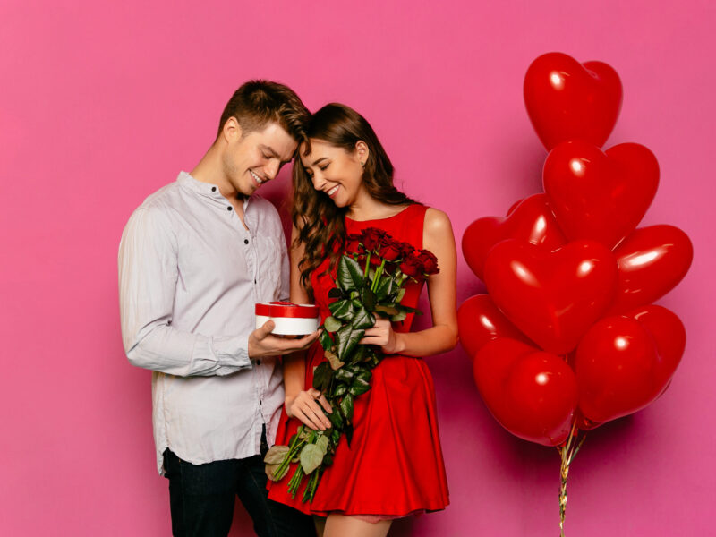 handsome-man-attractive-woman-looking-box-with-gift-red-roses